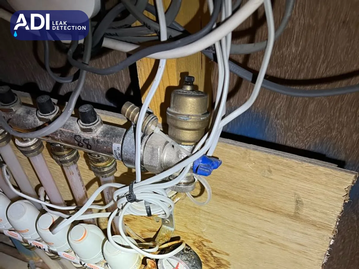 An underfloor heating manifold with a brass automatic air vent, among wiring